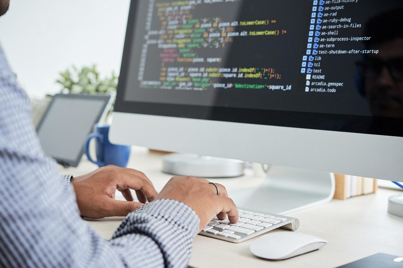 A developer typing at a desktop computer showing source code